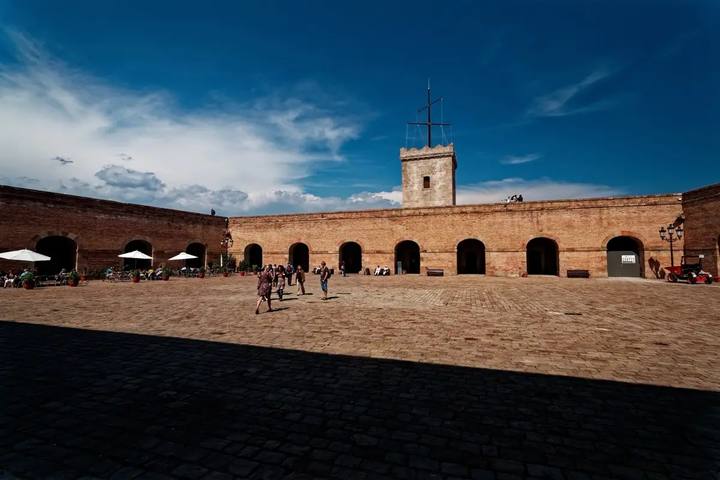 El patio de armas empedrado del castillo de Montjuïc, con sus muros de ladrillo y la torre de vigía bajo un cielo azul