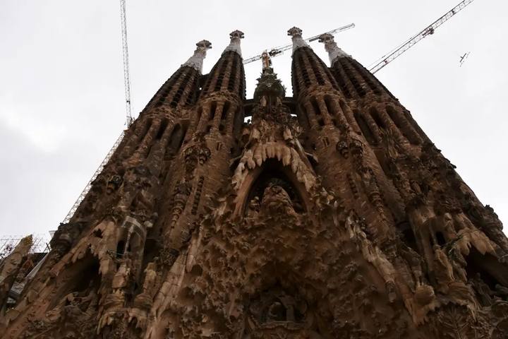 La fachada del Nacimiento de la Sagrada Familia vista desde abajo, con sus torres de piedra y dos grúas de las obras