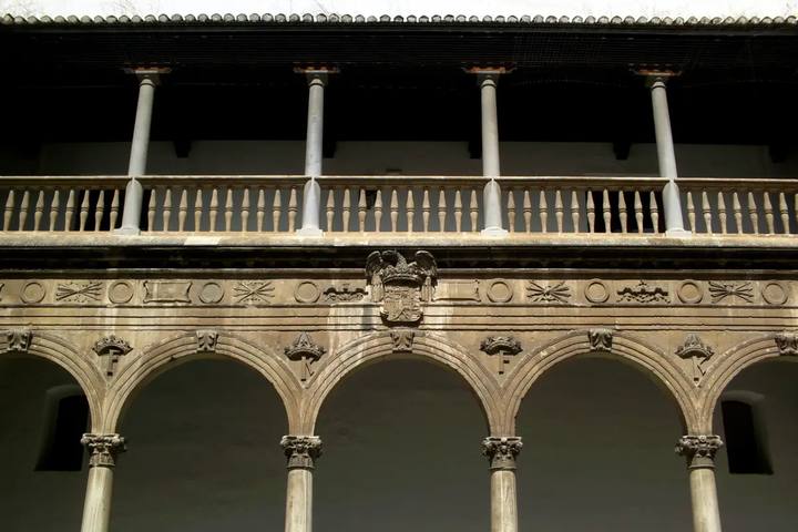 Galería de arcos y balaustrada con el escudo imperial en un patio del Hospital Real de Granada