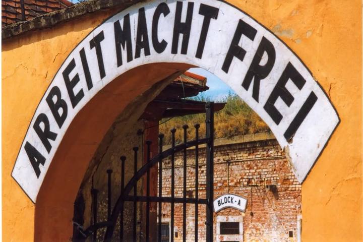 La puerta de la Pequeña Fortaleza de Terezín, con la inscripción «Arbeit macht frei» sobre el arco y la reja del bloque A detrás