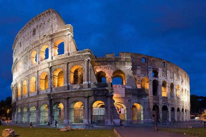 El Coliseo de Roma iluminado al anochecer, con sus arcos de piedra encendidos bajo un cielo azul intenso