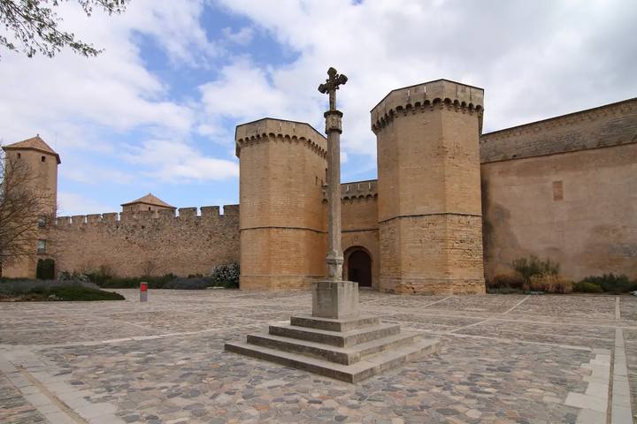 Puerta Real del Monasterio de Poblet entre dos torres almenadas, con la plaza empedrada y un crucero de piedra delante