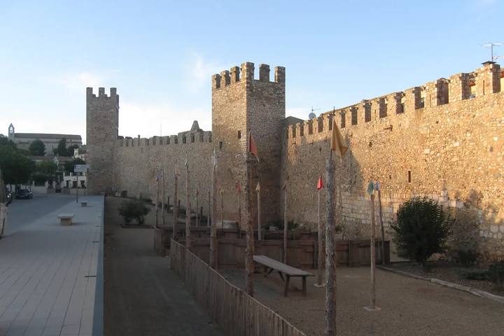 Murallas medievales de Montblanc con torres almenadas iluminadas por el sol de la tarde y banderolas en el foso