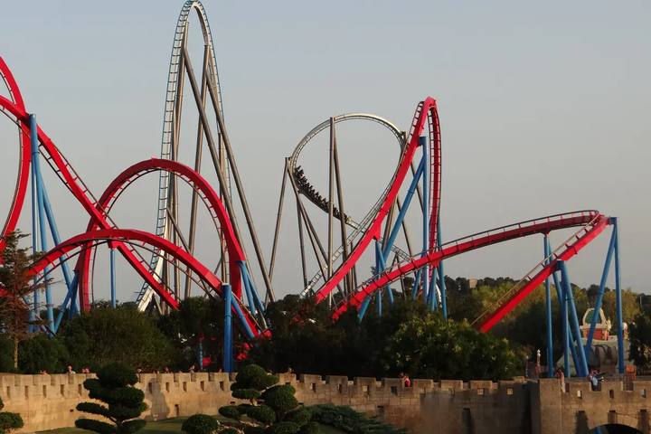 Montañas rusas Shambhala y Dragon Khan de PortAventura Park con sus vías rojas y grises sobre una muralla de piedra al atardecer