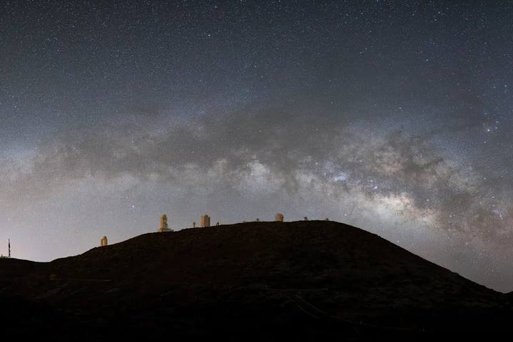 La Vía Láctea sobre la silueta de la loma del Observatorio del Teide, con las cúpulas iluminadas en el horizonte