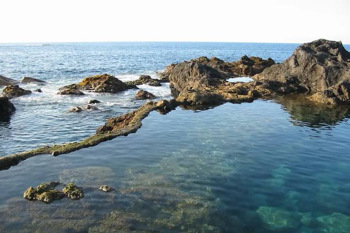 Charcos naturales de agua transparente entre rocas volcánicas en El Caletón de Garachico, con el mar abierto detrás