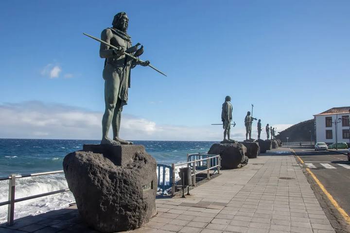 Estatuas de bronce de los menceyes guanches sobre pedestales de roca volcánica en el paseo marítimo de Candelaria, con el mar al fondo