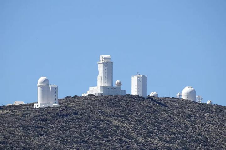 Cúpulas y torres blancas de los telescopios del Observatorio del Teide sobre una loma volcánica