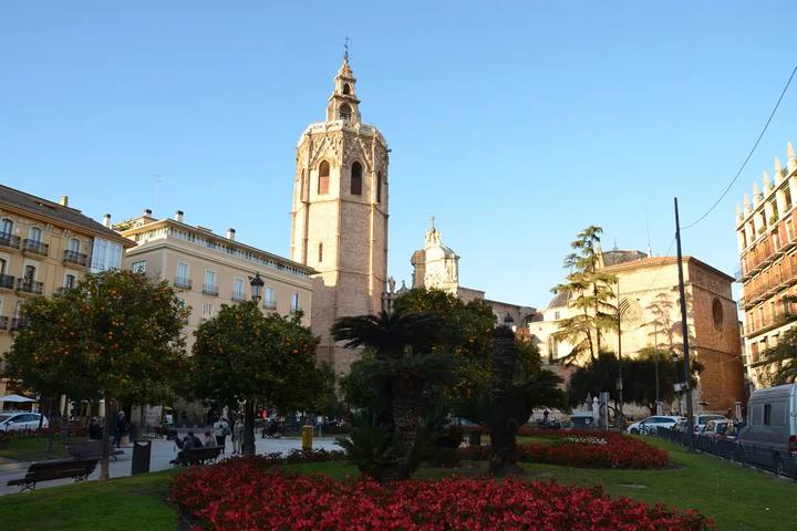 Torre del Micalet de la Catedral de Valencia vista desde la plaza de la Reina, con naranjos y parterres de flores rojas