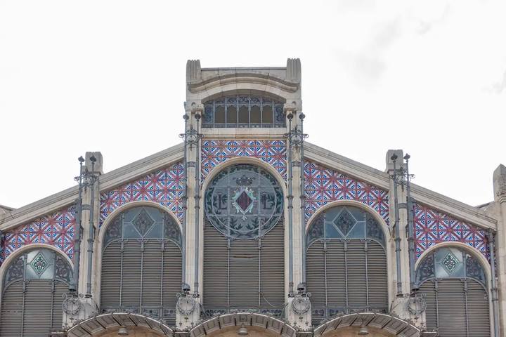 Fachada modernista del Mercado Central de Valencia con arcos, vidrieras y azulejos azules y rojos bajo cielo nublado