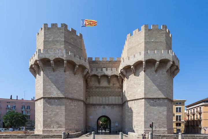 Torres de Serranos, puerta medieval de Valencia de dos torres almenadas con la senyera ondeando sobre un cielo azul